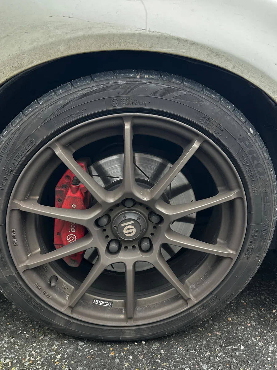 Before: Wheel and tyre clean by JJ Valets on a white car with Sparco wheels and red Brembo calipers: grimy wheel before and clean wheel with dressed tyre after